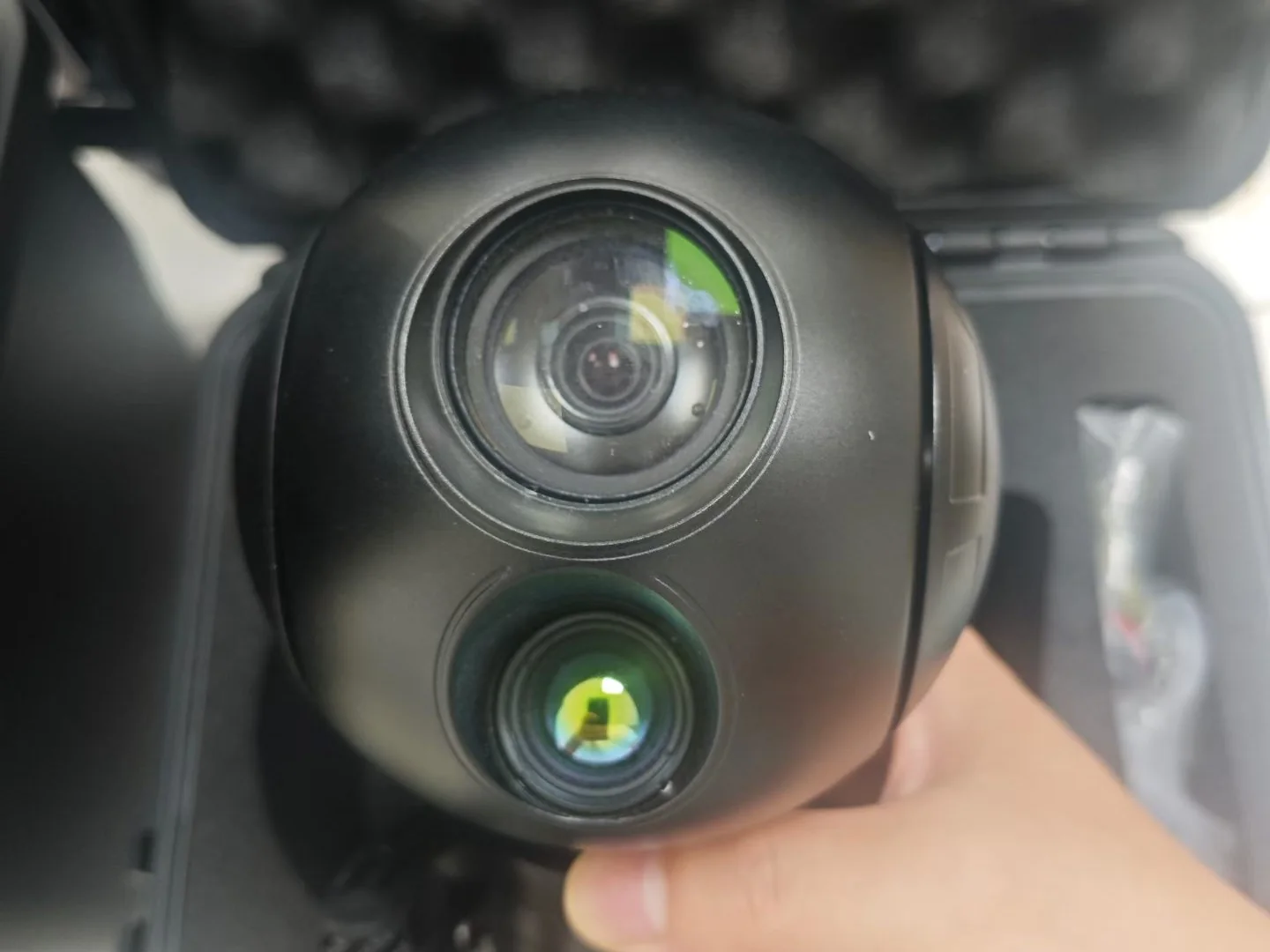 Black two-axis gimbal camera payload with a coated daylight lens, held in hand