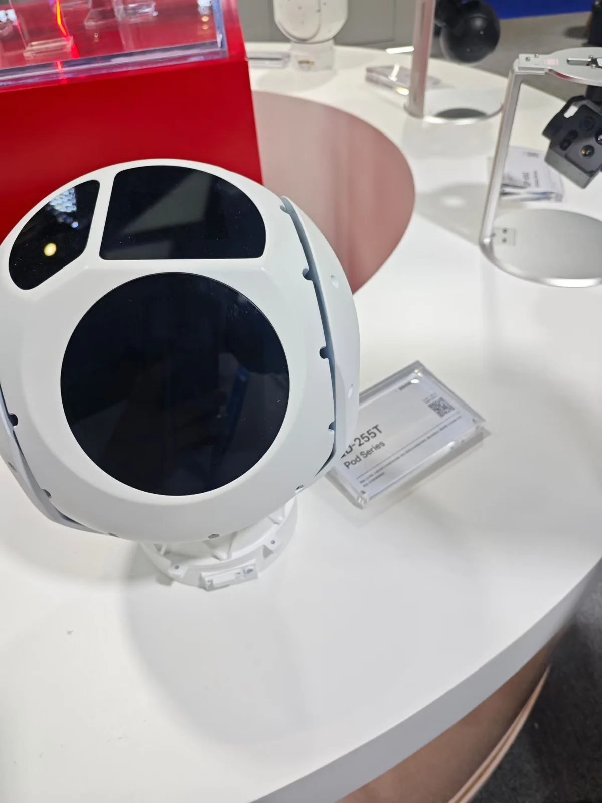 White stabilised EO/IR gimbal camera payload on its display stand